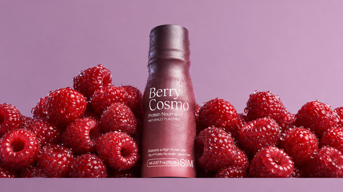 A bottle of Nouri-Shot Berry Cosmo flavored protein shot stands upright in the center, surrounded by fresh red raspberries on a solid lavender-purple background.