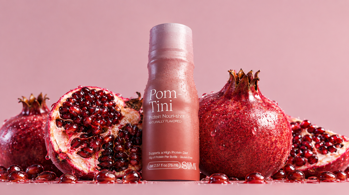 A bottle of Pom Tini Pomegranate Nourishing Protein Shot stands upright in the center, surrounded by fresh whole and halved pomegranates with scattered seeds on a pink background.

Details